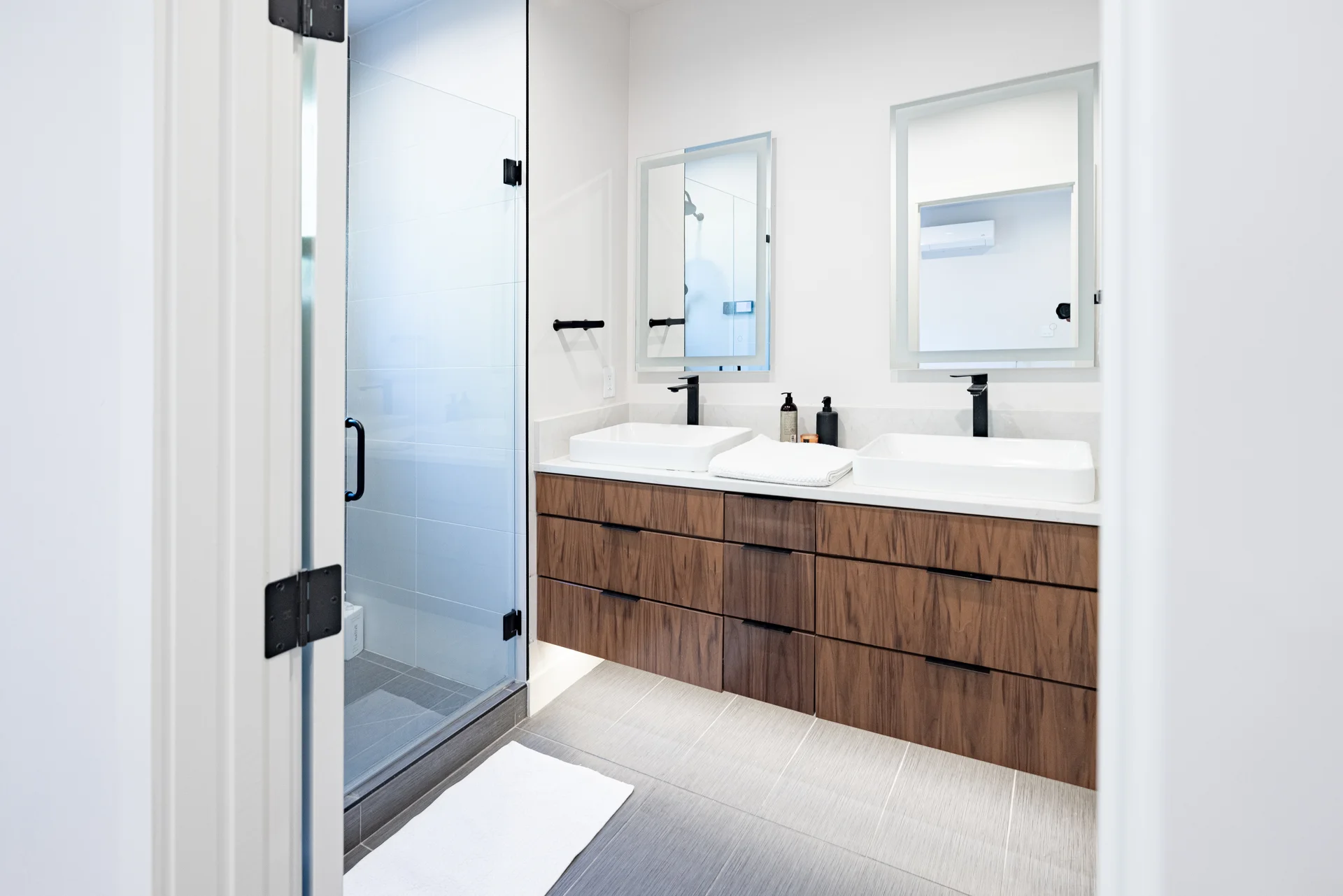 Modern bathroom with dual sinks, walnut floating vanity, and frameless glass shower enclosure