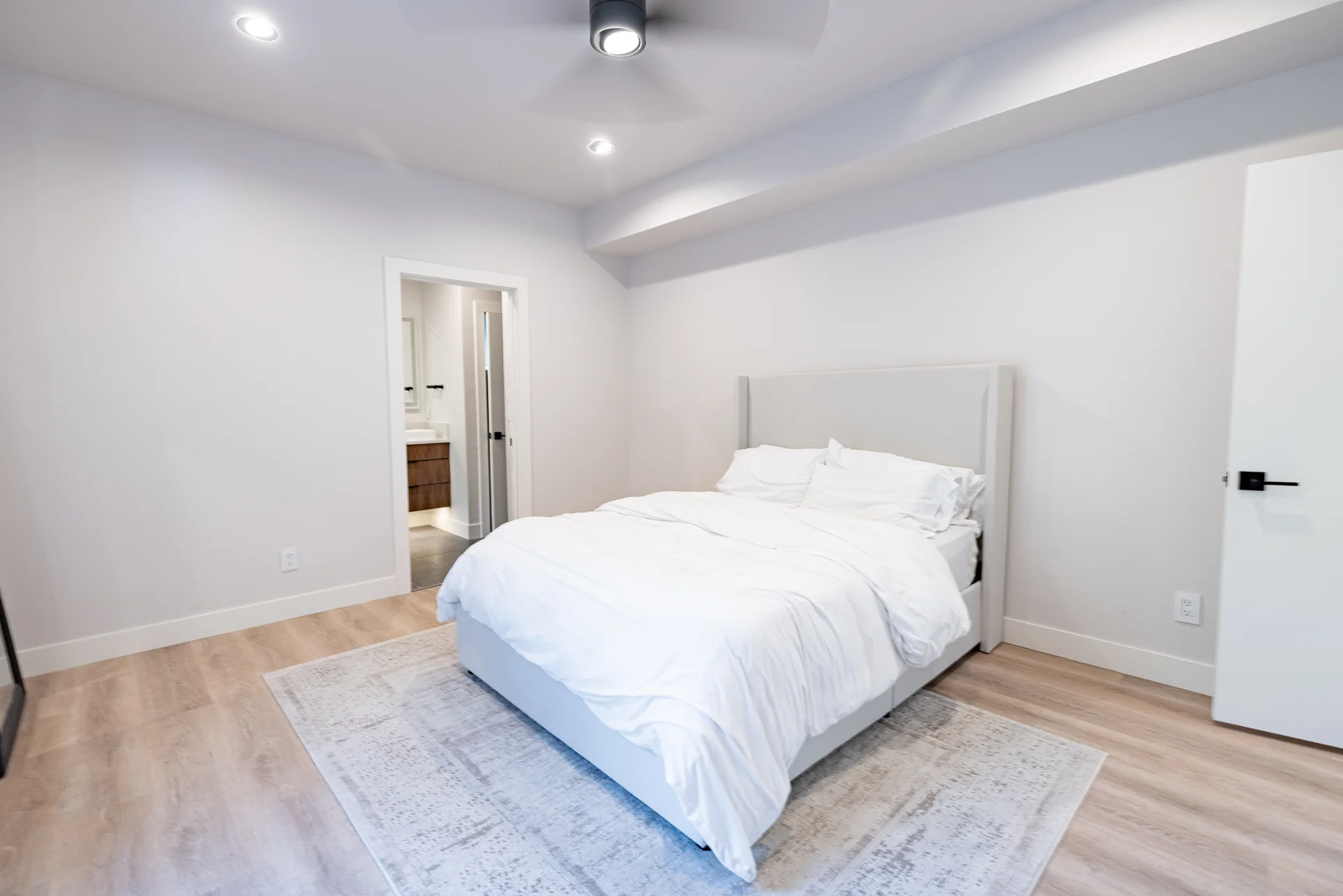 Primary bedroom with upholstered headboard, ceiling fan, and en-suite bathroom access