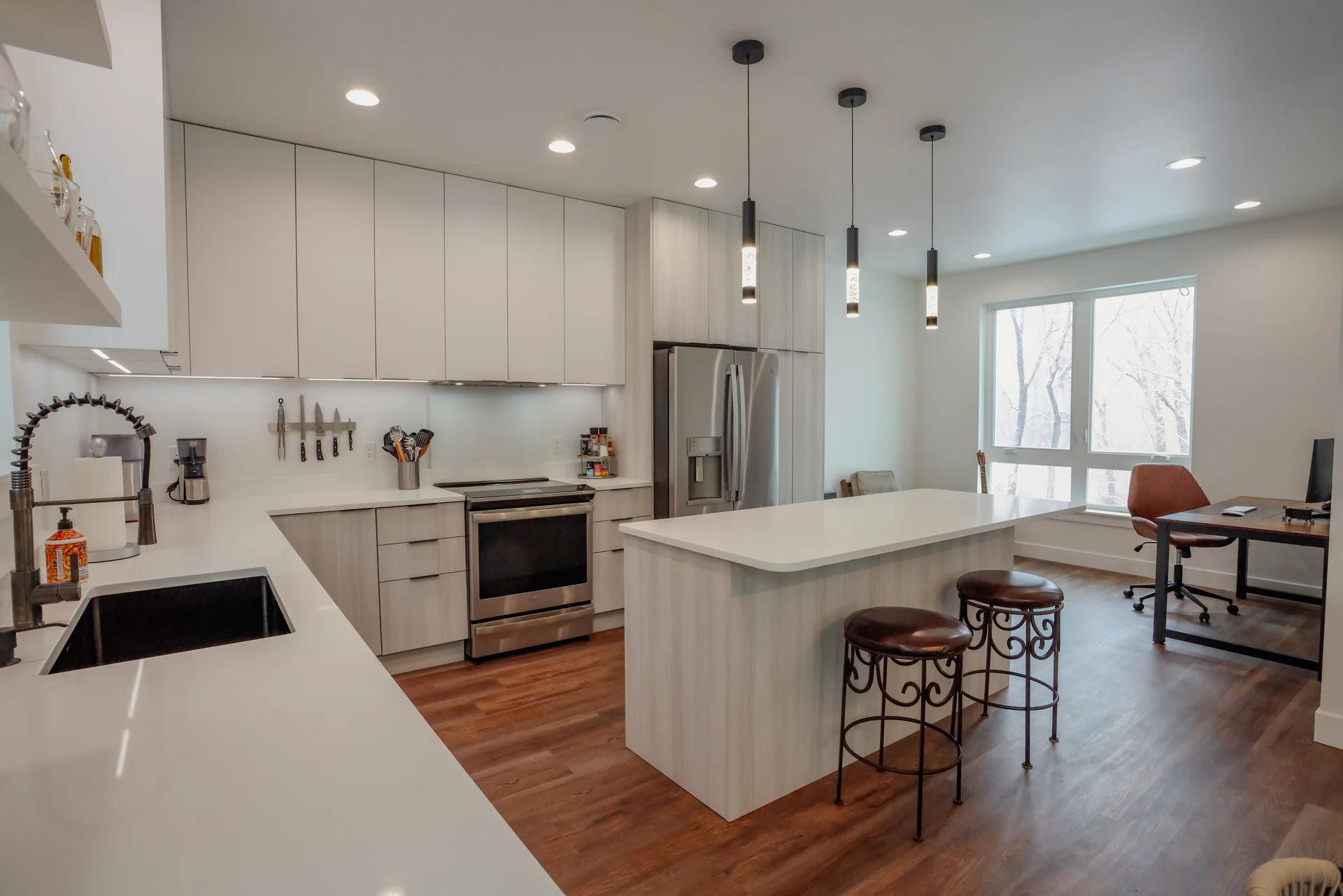 Open kitchen with white cabinetry, center island seating, pendant lights, and stainless appliances