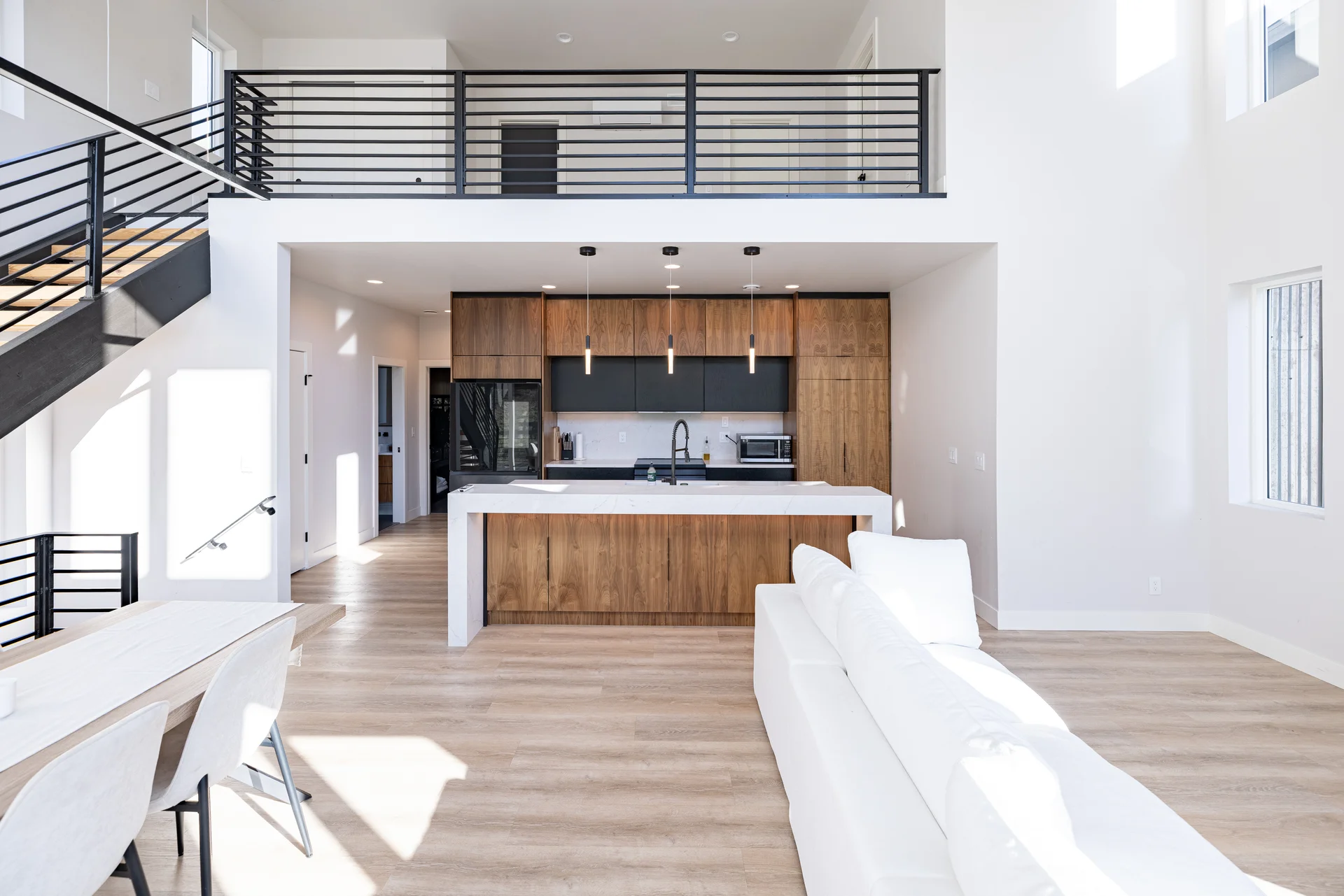 Two-story great room with open floor plan, modern staircase, and kitchen in background